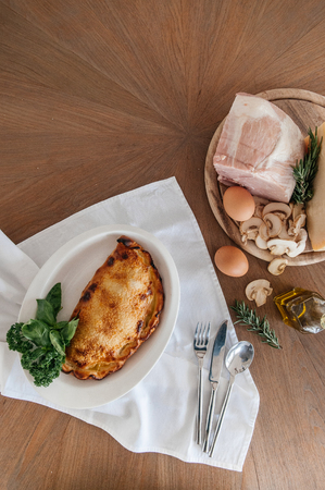 Ham cheese mushroom Calzone pizza with raw ingredients eggs, Champignon mushroom, Parmigiano cheese, Ham, olive oil on wood table with silverware. Top viewの写真素材