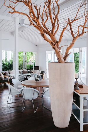 AUG 7, 2014 Hua Hin, Thailand - Tropical modern beach house white tone wood floor living room interior with so many decorating items, well design chairs and table with oversized stone vase with dried tree branches.のeditorial素材