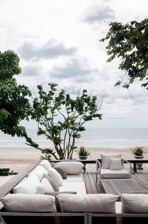 AUG 7, 2014 Hua Hin, Thailand - Tropical vacation. seaview wooden balcony with white fabric sofa couch and pillows under lush green tree and tropical plants bush.のeditorial素材