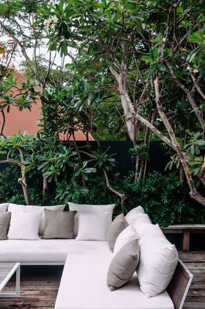 AUG 7, 2014 Hua Hin, Thailand -  Tropical vacation wooden balcony with white fabric sofa couch and pillows under lush green tree and tropical plants bush.のeditorial素材