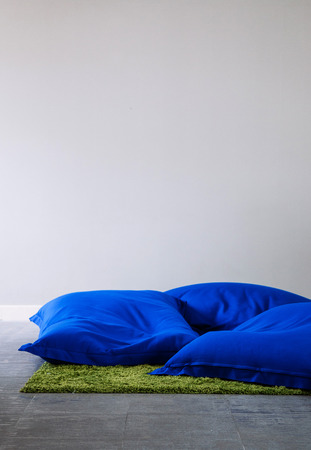 Blue bean bags on concrete floor with green carpet rug and white wall copy space background.の写真素材