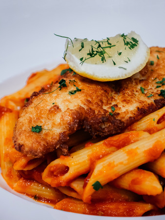 Penne pomodoro pasta with crispy fried fisb fillet top with lemon and parsley. Close up shotの写真素材