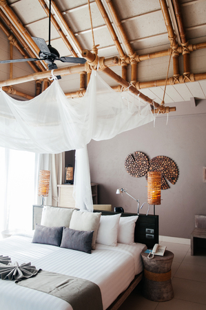 MAY 21, 2014 Krabi, THAILAND - Asian Thai tropical luxury resort room with wooden bed and white curtain and bamboo floor lamps. High ceiling hotel room interior.のeditorial素材