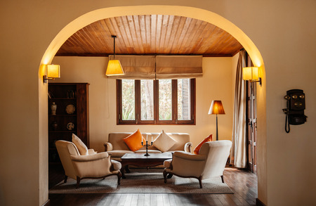 FEB 25, 2014 Dalat, Vietnam - Vintage colonial tropical living room hard wood floor and ceiling with sofa couch, classic lamps and curtain. Furnished with wooden coffee table, colourful pillows and retro telephoneのeditorial素材