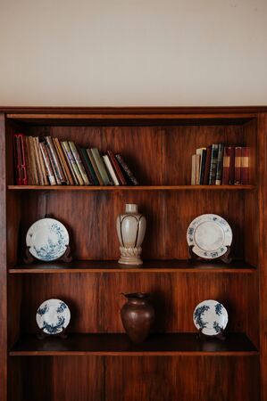Wooden bookshelf with old books and blue pattern vintage Chinaware plates, Ceramic Vase and copper jarの写真素材