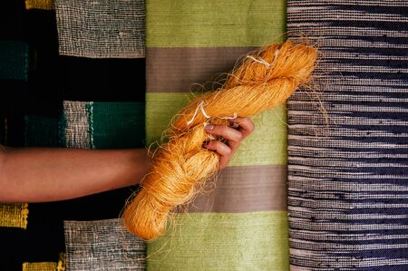 Hand holding natural yellow silk thread fiber. Raw material of traditional sericulture Thai silk...