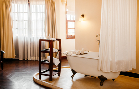 FEB 25 Dalat, Vietnam - Warm atmosphere old vintage colonial bathroom with white retro clawfoot bathtub with white curtain and wooden towels shelf on terrazzo floorのeditorial素材