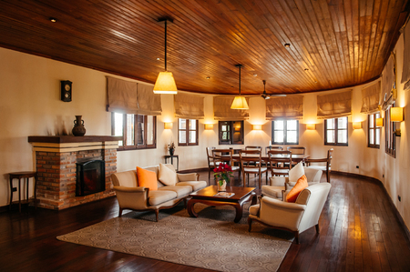 FEB 25, 2014 Dalat, Vietnam - Vintage colonial living room hard wood floor and ceiling with sofa couch, armchairs. Furnished with old wood coffee table, colourful pillows, retro clock and fireplaceのeditorial素材
