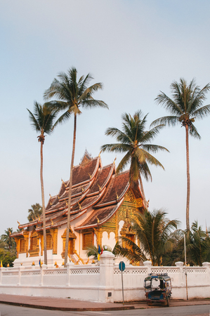 Luang Prabang, Laos - Luang Prabang Royal Palace Museum and Hor Prabang temple hall under coconut tree with Tuk Tuk park at wall side and morning quiet streetのeditorial素材