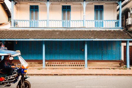 APR 4, 2019 Luang Prabang, Laos - blue door French Colonial building and colourful Tuk Tuk Skylab on main street - Famous transport type among touristのeditorial素材