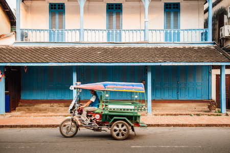 APR 4, 2019 Luang Prabang, Laos - blue door French Colonial building and colourful Tuk Tuk Skylab on main street - Famous transport type among touristのeditorial素材