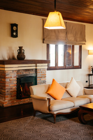 FEB 25, 2014 Dalat, Vietnam - Vintage colonial living room hard wood floor and ceiling with sofa couch, armchairs. Furnished with old wood coffee table, colourful pillows, retro clock and fireplaceのeditorial素材