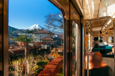 Fujiyoshida, Japan - NOV 30, 2018 : Snow covered Mount Fuji behind local town along train route from Tokyo to Kawaguchiko seen through train window with tourist sit at seat.のeditorial素材