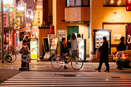 Tokyo, Japan - NOVEMBER 29, 2018 : Night street with shops and neon signs with people walking, riding bicycle waiting for traffic light in Asakusa district.のeditorial素材