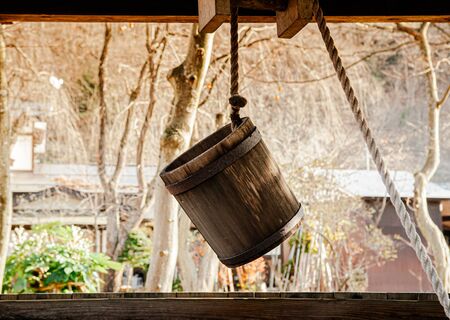 Old antique Water well wooden bucket with rope hanging above the holeの写真素材