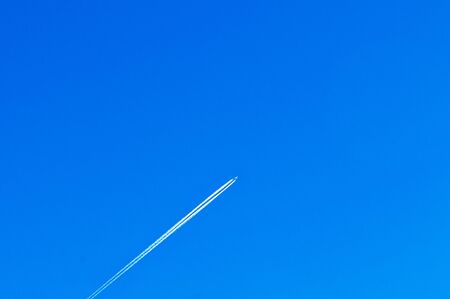 Airplane white smoke contrail tail at high speed cuising at high speed in blue winter sky