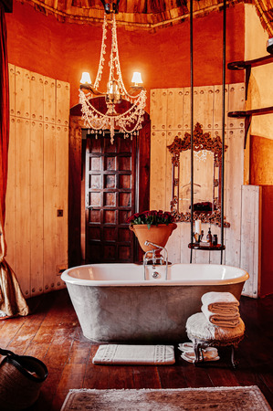 JUN 23, 2011 Ngorongoro, Tanzania - Luxury African tribal hut bathroom interior decoration with old vintage ceramic bathtub and chandelier with colonial furniture and glamourous ornaments under warm lightのeditorial素材