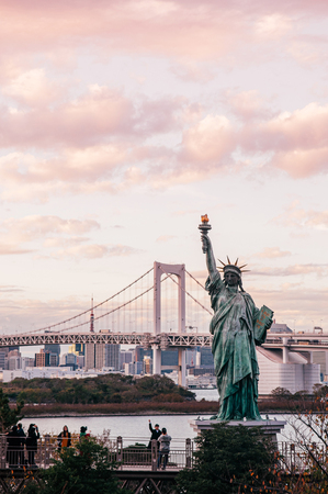 DEC 5, 2019 Tokyo, Japan - Odaiba Rainbow bridge and Tokyo bay view with tourists enjoy evening sunset with cityscape in background under warm tone skyのeditorial素材