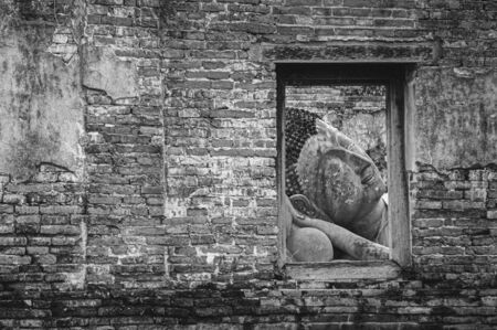 Ayutthaya ancient ruined Buddha statue seen through window frame on brick wall of Wat Putthaisawan temple - Thailandの写真素材