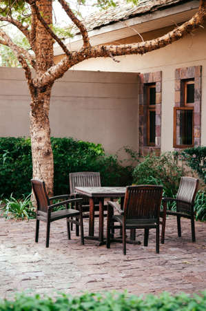 JUN 19, 2011 Serengeti, Tanzania -  - Old wooden chairs and table set in tropical backyard garden under tree with green shrubs under natural light in the afternoonのeditorial素材