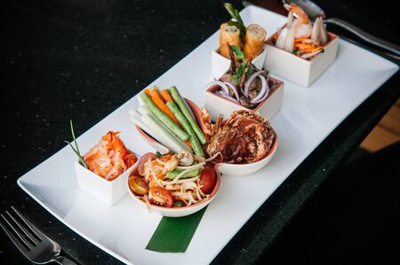 Thailand local street cuisine, spicy papaya salad or Som Tum with deep fried soft shell crab and spring rolls on white dishの写真素材
