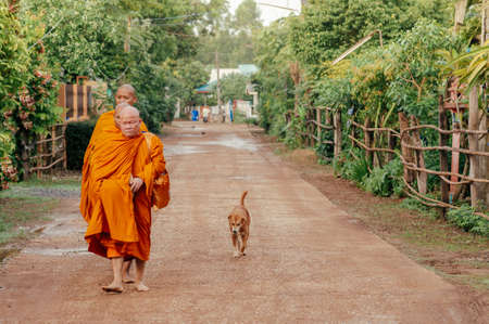 MAY 31, 2018 Sa Kaeo, Thailand - Thai Buddhist Monks walk along peaceful village road for morning alms following by street dogのeditorial素材
