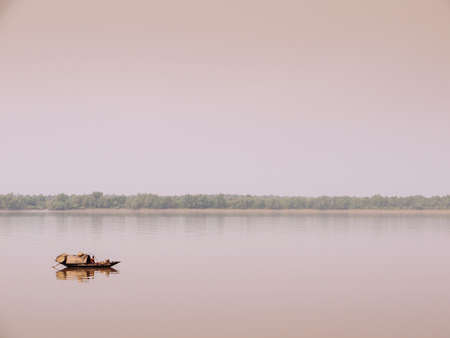 FEB 15, 2012 Dhaka, Bangladesh - Bangladesh local people on wooden row boat in peaceful river with tropical mangrove forest in evening before sunsetのeditorial素材