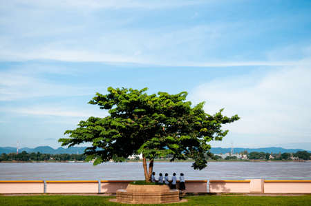 SEP 14, 2012 Nakhon Phanom, Thailand - Mae Khong river in Nakhon Phanom. Natural border between Thailand and Laos with Asian kids standing under big tree. Peaceful scenery