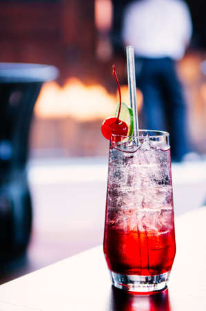 Fresh ice cold sparkling cherry lime cocktail with ice cubes in clear glass on table.