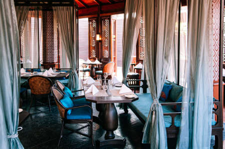 MAR 5, 2012 Chiang Mai, Thailand - Vintage antique teak wood armchairs, couch and dining table. Asian comtemporary restaurant interior with natural lightのeditorial素材