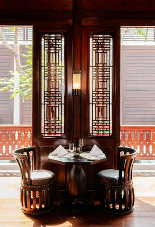 MAR 5, 2012 Chiang Mai, Thailand - Vintage antique teak wood armchairs, couch and dining table. Asian comtemporary restaurant interior with natural afternoon lightのeditorial素材