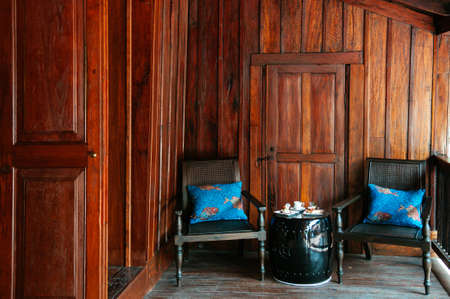 MAR 5, 2012 Chiang Mai, Thailand - Vintage antique teak wood armchairs and coffee table in Asian comtemporary wooden house with natural lightのeditorial素材