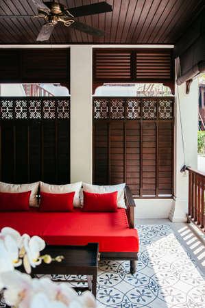 MAR 5, 2012 Chiang Mai, Thailand - Red couch seat on Asian comtemporary patio leisure and resting area with White Phalaenopsis orchid in foregroundのeditorial素材