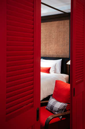 MAR 5, 2012 Chiang Mai, Thailand - Resort style bedroom with red armchair and white bed seen through red doors, Asian comtemporary bedroom decorのeditorial素材