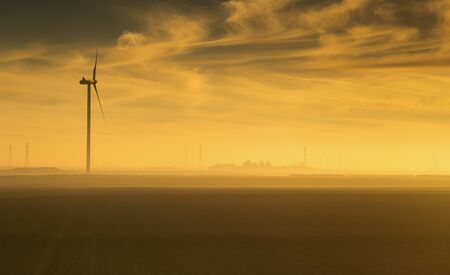 Single wind turbine captured at sunrise in the countryside of France with silhouettte of power poles...