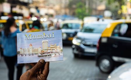 Hand with postcard booklet with Mumbai written on it shot with the blurred city in the background. A contrast in lifestylesの写真素材