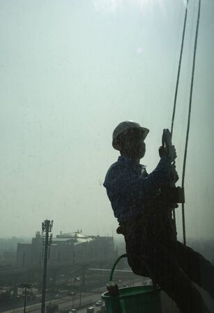 Silhouette of Window Cleaner hanging outside a building with dirty window in foreground