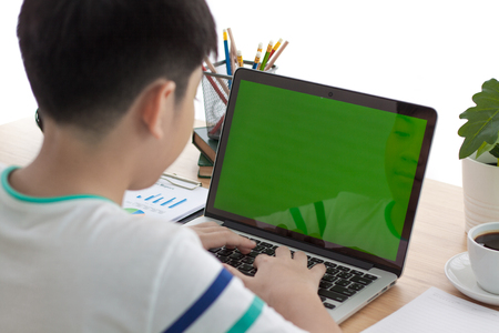 Over the shoulder shot of an Asain boy typing on a computer laptop with a key-green screen. Woman hand typing laptop with green screen.の写真素材