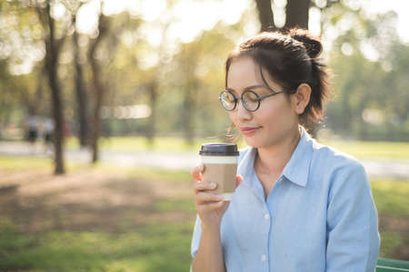 Asian woman drinking hot coffee with feeling happy in the green graden.