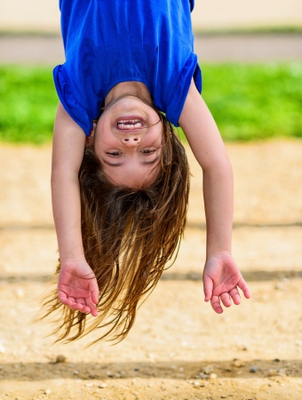 beautiful child hanging upside, laughing, with greenery in the backgroundの写真素材