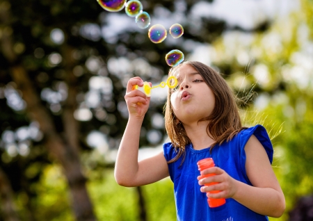 beautiful child blowing bubbles in a meadow  with greenery in the backgroundの写真素材