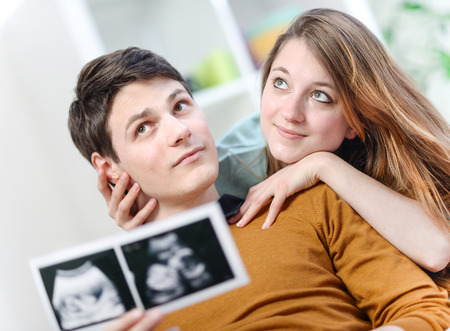 Beautiful couple imagines the future of their unborn child with ultrasound pictures in handsの写真素材