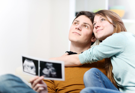 Beautiful couple imagines the future of their unborn child with ultrasound pictures in handsの写真素材