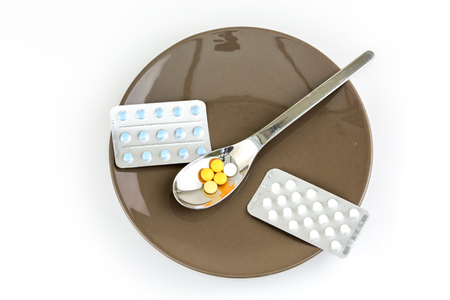 Still life on a plate with colorful pills in blishter packs and on a tea spoon with white backgroundの写真素材