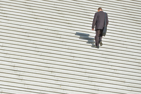 A man in business clothing climbing up along large endless stairの写真素材