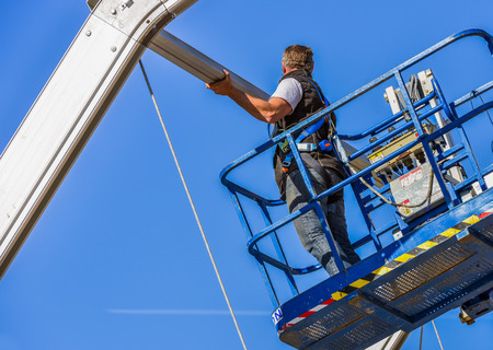 Construction worker fastening roof ridge on skylift with clear blue sky in the backgroundの写真素材