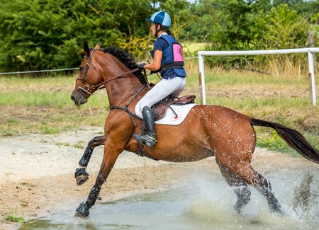 Saint Cyr du Doret, France - July 29, 2016: Rider crossing water jump galloping at a cross country manisfestationのeditorial素材