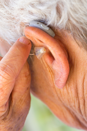 closeup senior woman inserting hearing aid in her earsの写真素材
