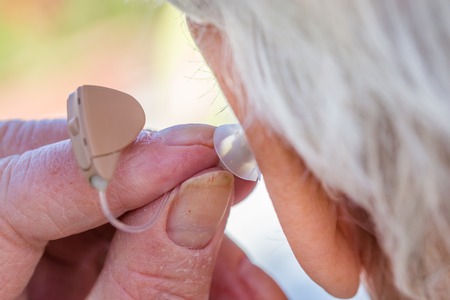 closeup senior woman inserting hearing aid in her earsの写真素材