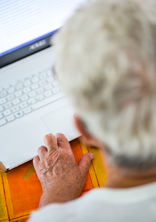 Closeup on pair of old hands typing on a laptop ontop of a desk.